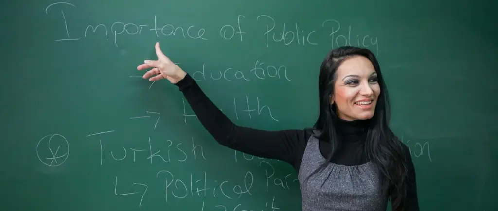 محاضِرة أمام السبورة في برنامج الإدارة العامة بجامعة شرق البحر المتوسط، وعليها مخطط أهمية السياسات العامة في التعليم والصحة